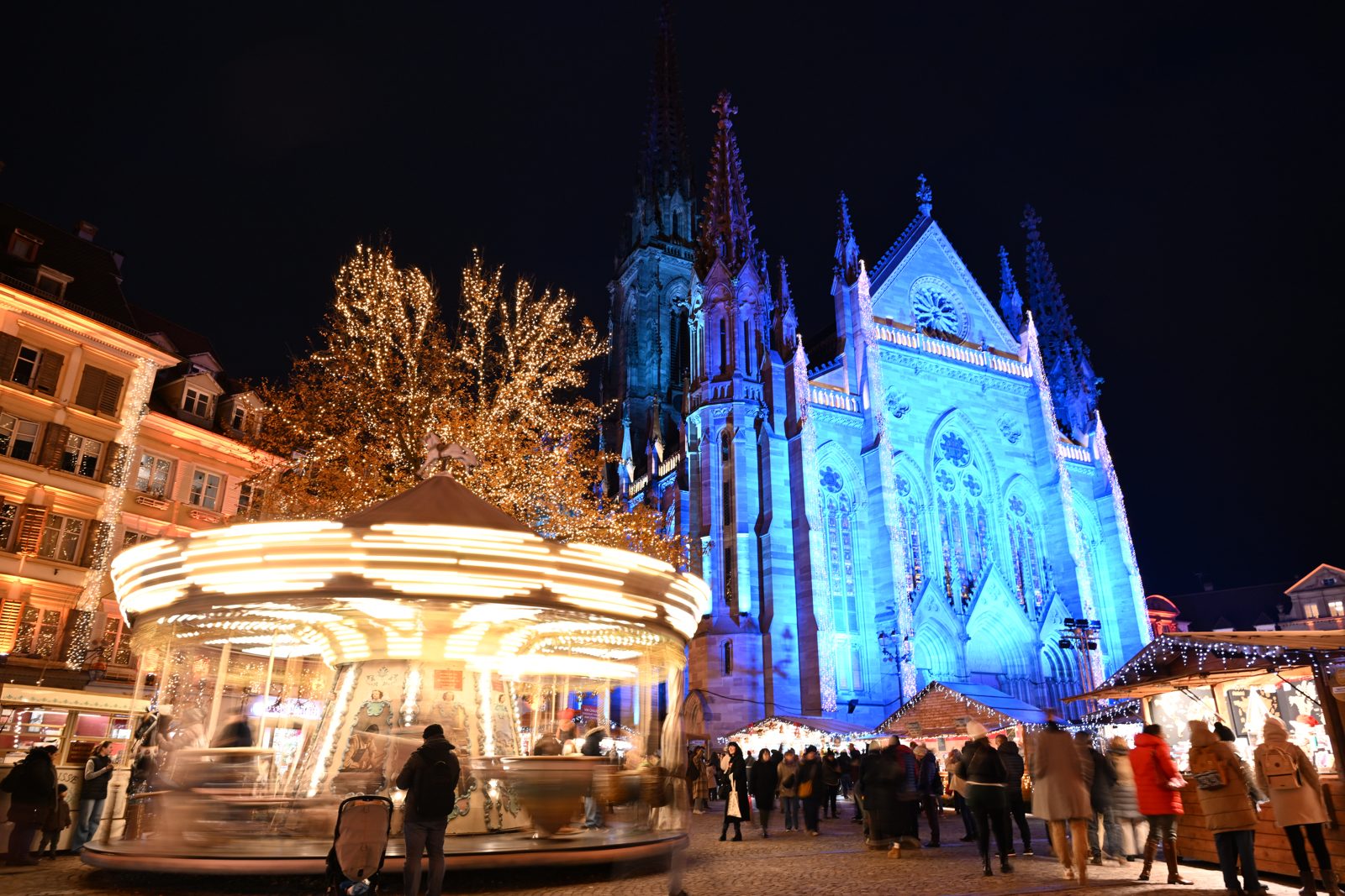 Karussell und der beleuchtete Temple Saint-Étienne auf dem Weihnachtsmarkt Mulhouse am Abend
