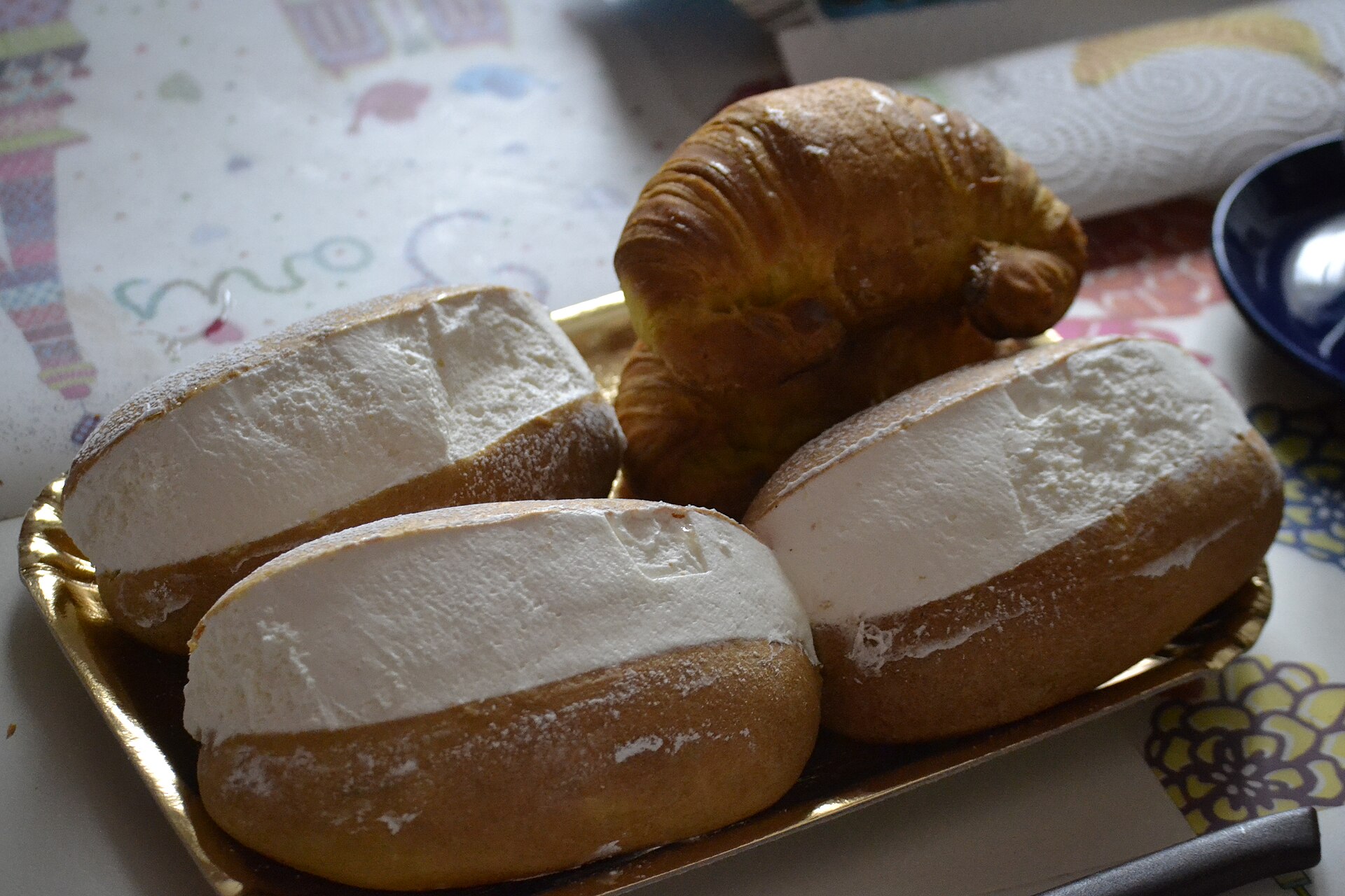 Drei mit Sahne gefüllte Maritozzi und ein Cornetto auf einem goldenen Gebäcktablett