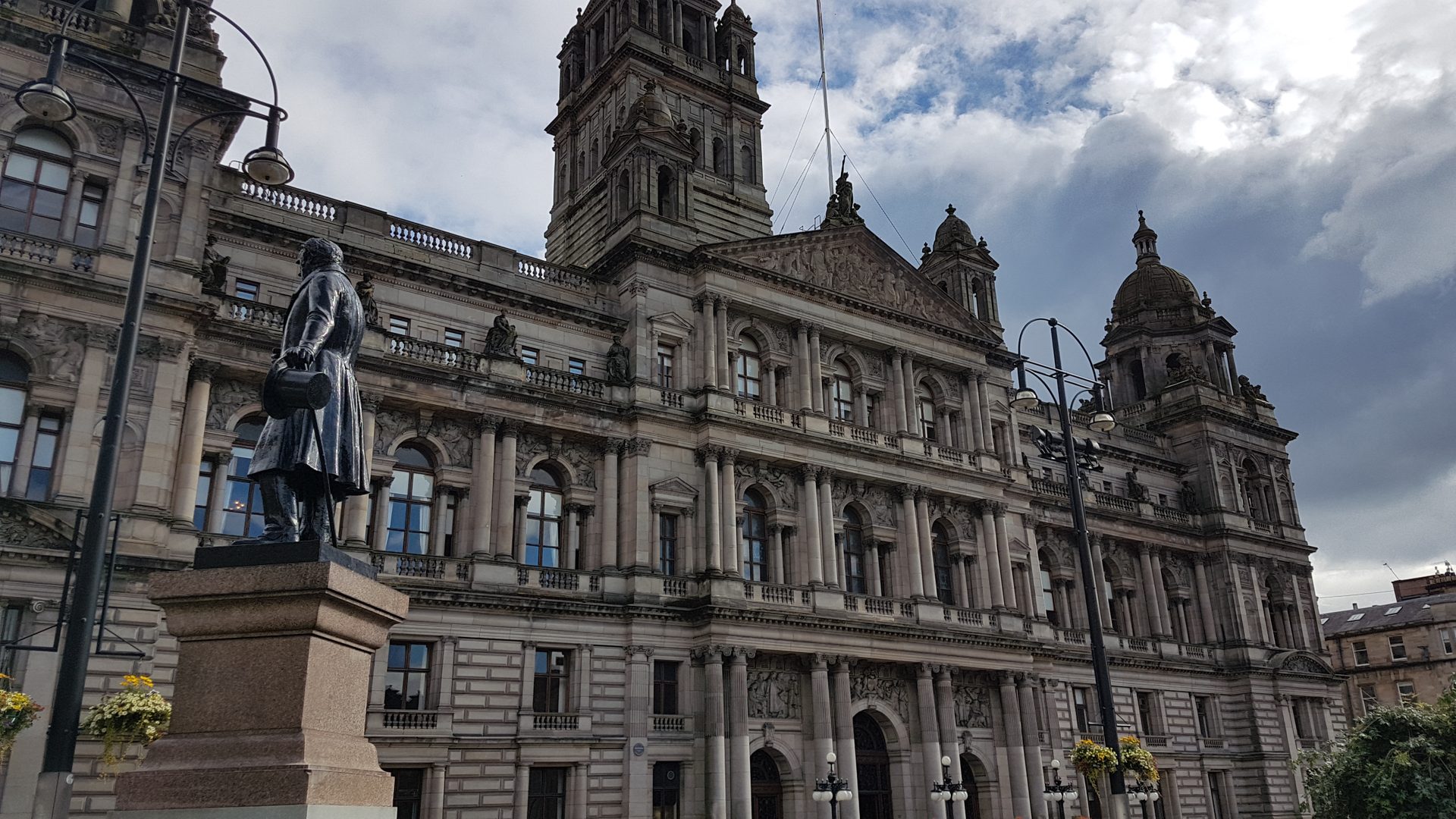 La facciata in pietra e le torri delle Glasgow City Chambers in George Square, con una statua davanti