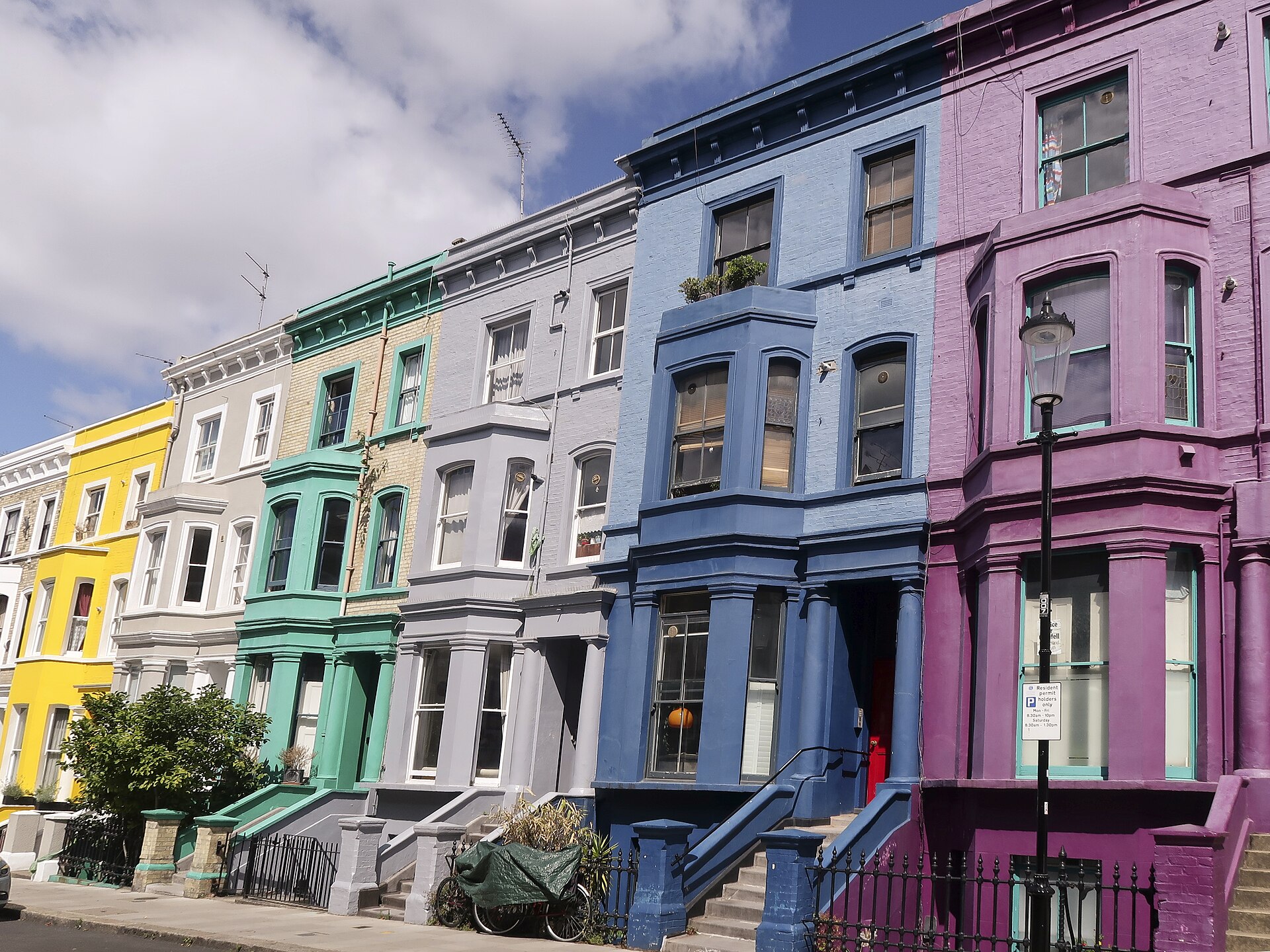 A row of terraced houses painted yellow, mint, grey, blue and purple on Lancaster Road, Notting Hill, London
