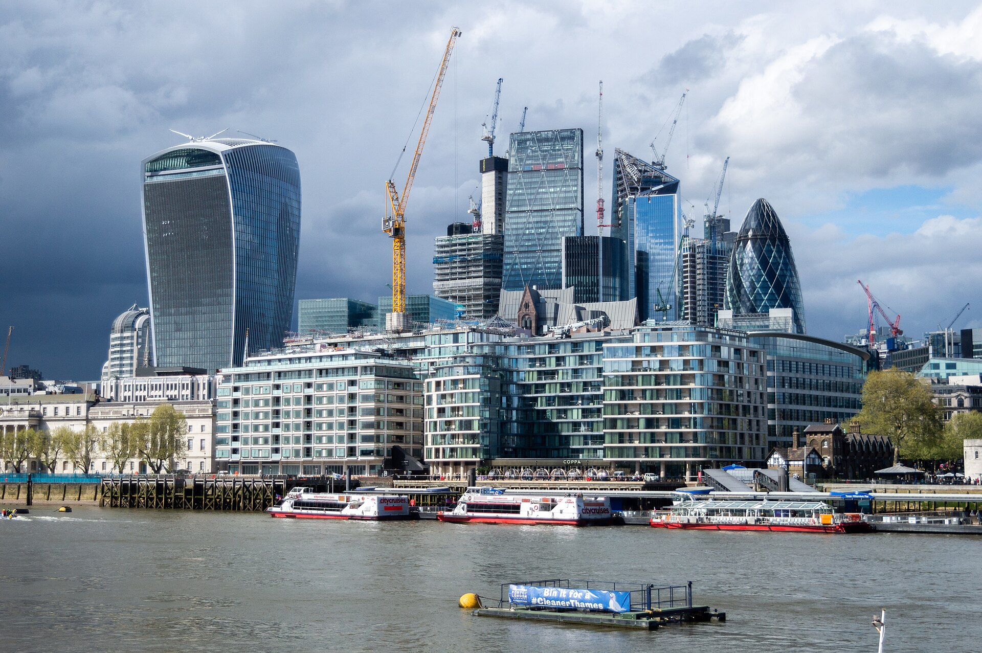 The City of London skyline across the River Thames, with tour boats moored along the riverbank