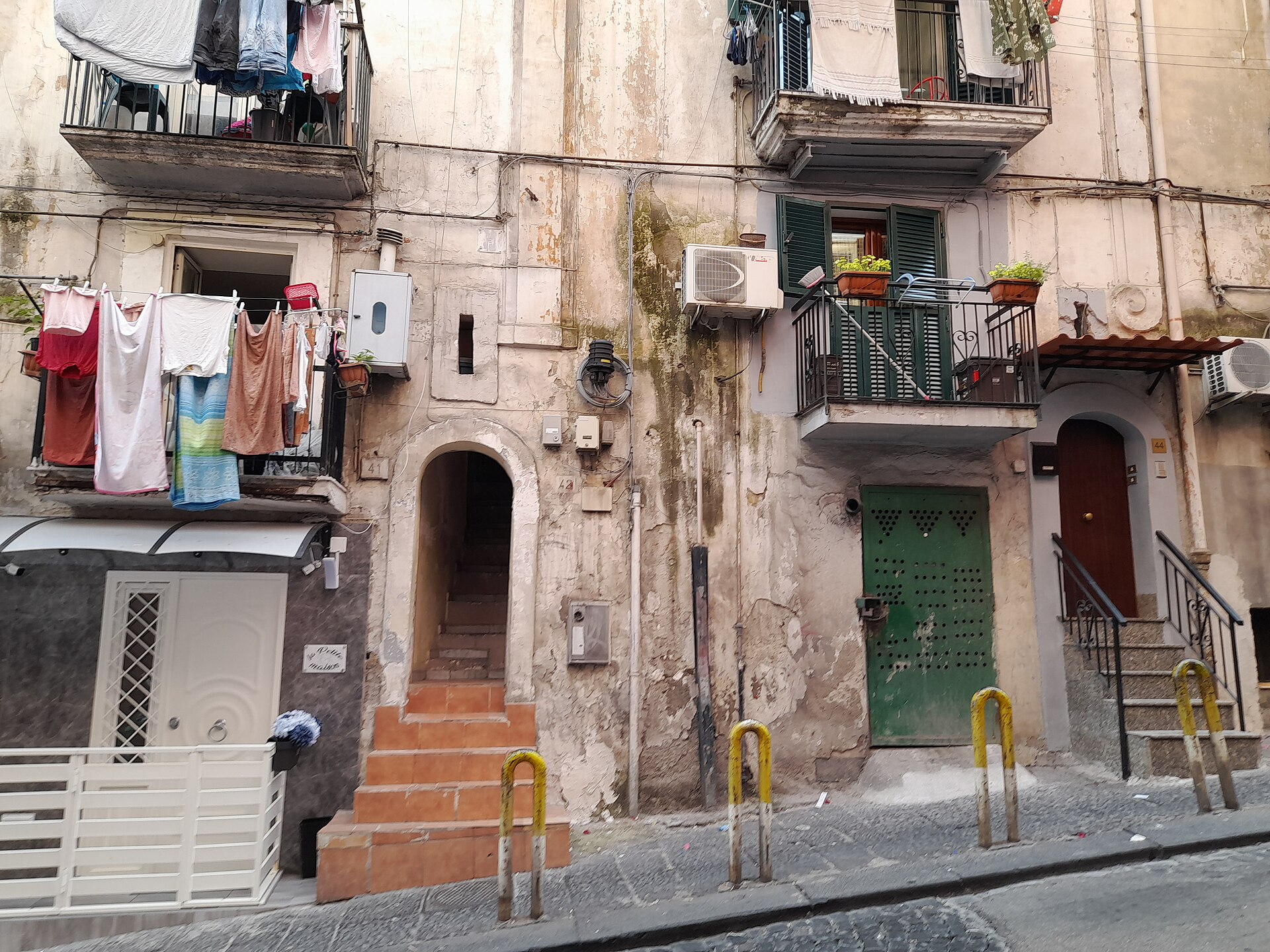 Un palazzo segnato dal tempo nei Quartieri Spagnoli di Napoli, con panni stesi ai balconi e gradini verso un portone ad arco