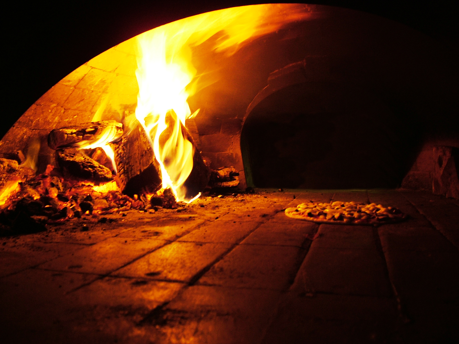 Flammen in einem Holzofen, auf dem Steinboden backt eine Pizza