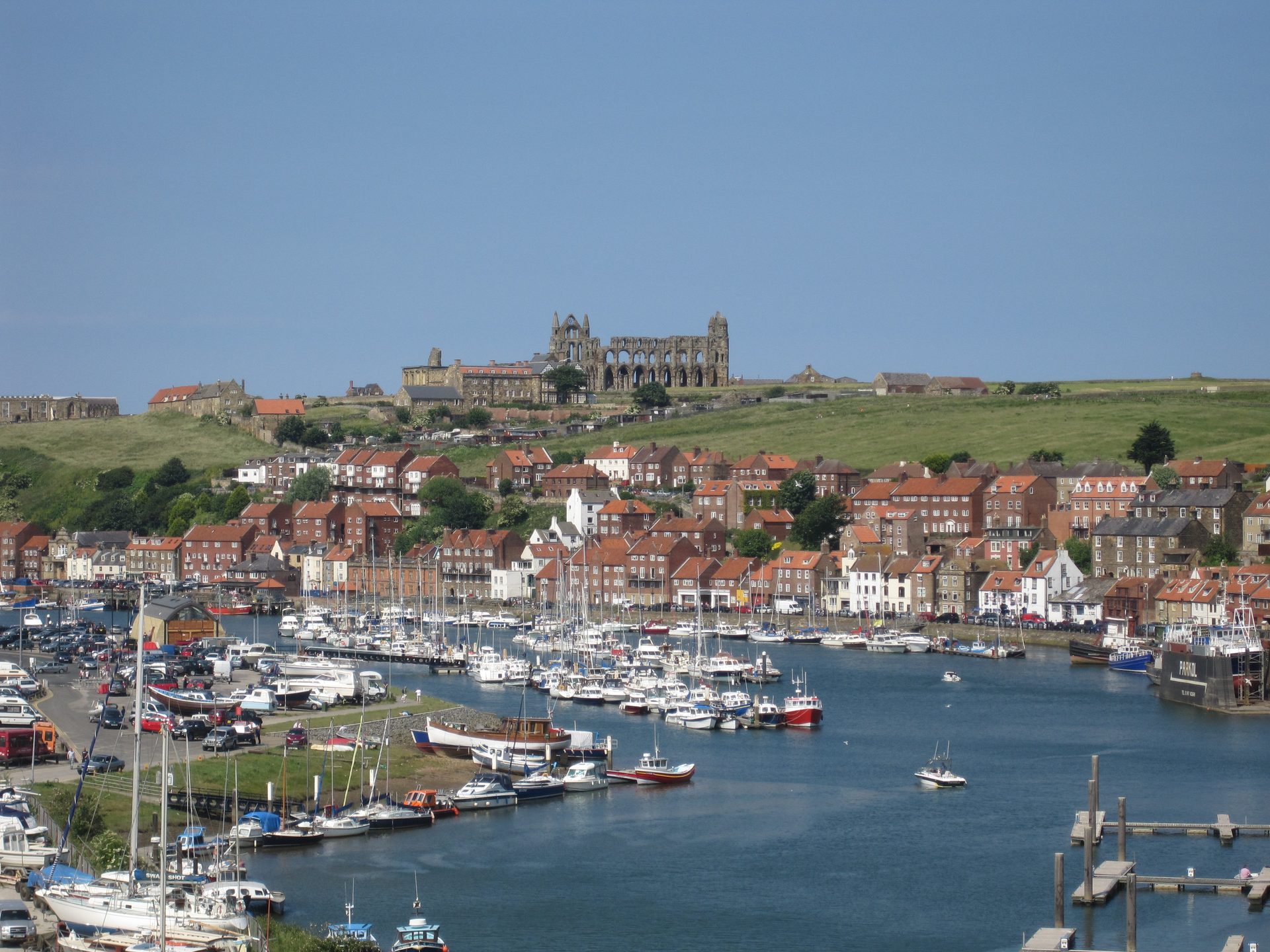 Il porto di Whitby pieno di barche sotto case dai tetti rossi, con le rovine dell'abbazia di Whitby sulla scogliera